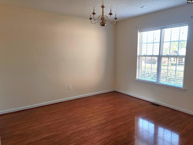 empty room with an inviting chandelier, hardwood / wood-style floors, and a textured ceiling