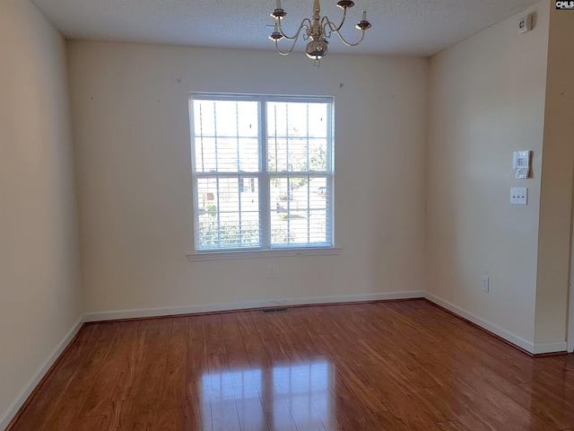 unfurnished room featuring an inviting chandelier, wood-type flooring, and a textured ceiling