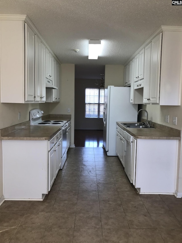 kitchen featuring sink, white appliances, a textured ceiling, white cabinets, and dark tile patterned flooring