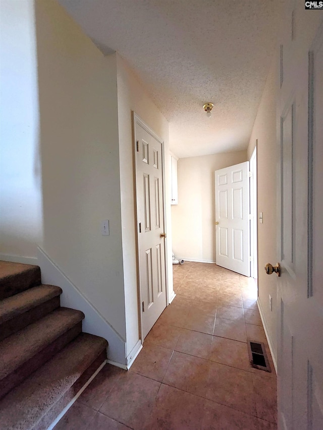 corridor featuring a textured ceiling and light tile patterned flooring