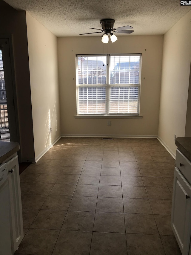 unfurnished dining area featuring a textured ceiling, dark tile patterned flooring, and ceiling fan