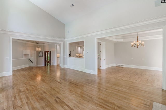 unfurnished living room with light hardwood / wood-style floors, a notable chandelier, ornamental molding, and a towering ceiling