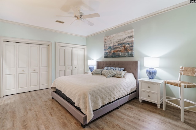 bedroom with multiple closets, light hardwood / wood-style flooring, ornamental molding, and ceiling fan