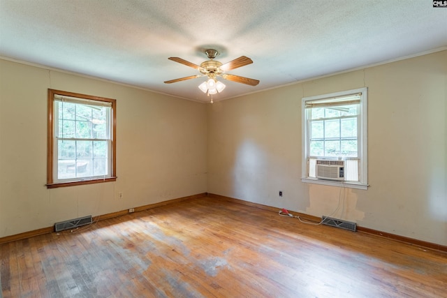 empty room with light wood-style flooring, a textured ceiling, visible vents, and cooling unit