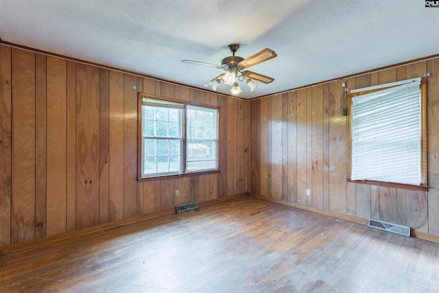 unfurnished room featuring ceiling fan, wood finished floors, visible vents, and wooden walls