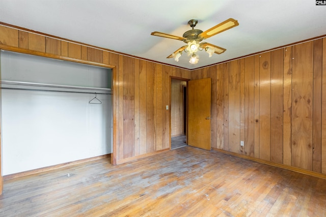 unfurnished bedroom with baseboards, hardwood / wood-style flooring, ceiling fan, wood walls, and a closet