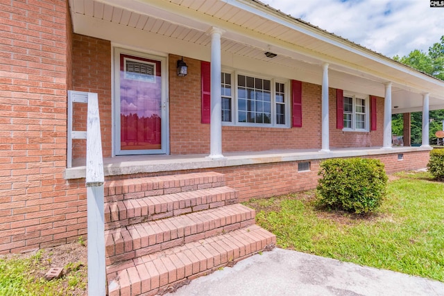 view of exterior entry with crawl space, brick siding, and covered porch