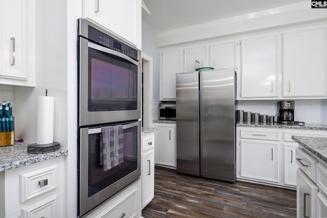 kitchen featuring light stone countertops, white cabinetry, stainless steel appliances, dark hardwood / wood-style floors, and backsplash