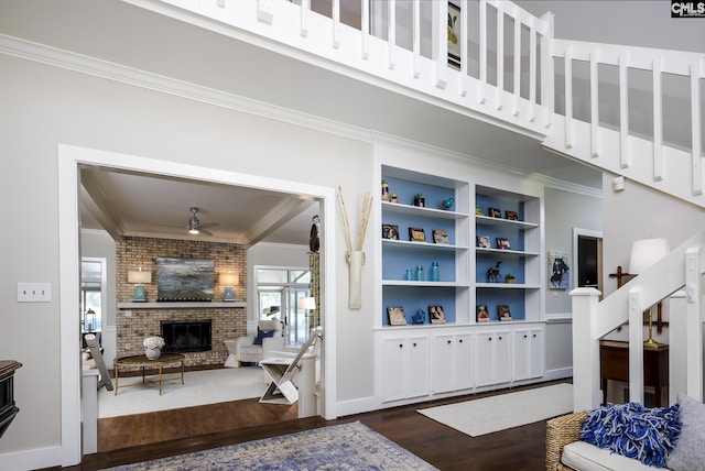 living room featuring built in shelves, ceiling fan, dark hardwood / wood-style flooring, brick wall, and a fireplace