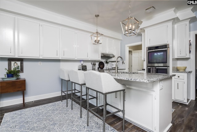 kitchen featuring a breakfast bar, stainless steel double oven, sink, pendant lighting, and white cabinets