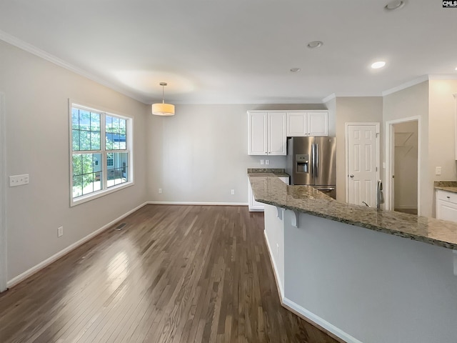 kitchen with light stone counters, dark hardwood / wood-style floors, decorative light fixtures, stainless steel fridge, and white cabinets