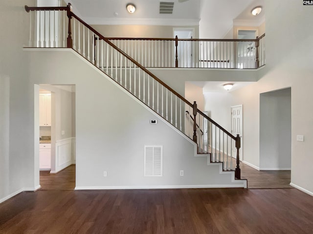 stairway featuring a high ceiling, ornamental molding, and hardwood / wood-style flooring