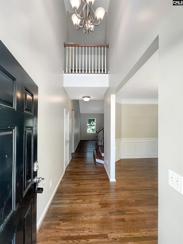 foyer featuring a high ceiling, dark wood-type flooring, an inviting chandelier, and crown molding