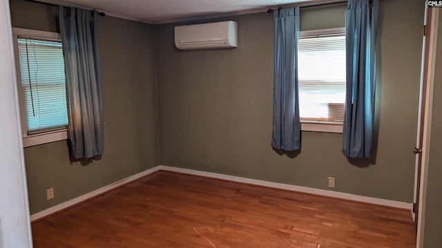 spare room featuring ornamental molding, a wall mounted AC, wood finished floors, and baseboards