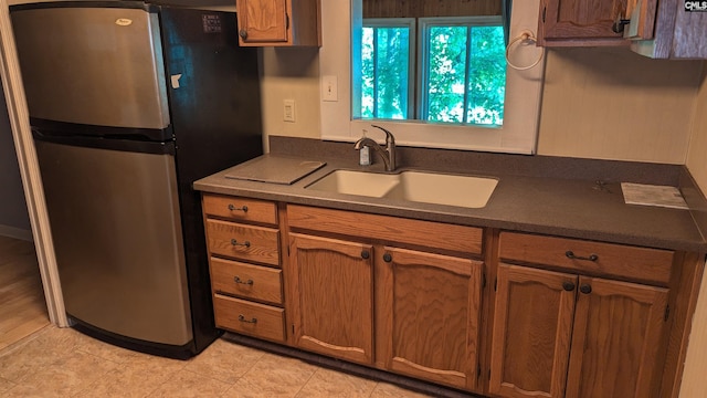 kitchen with dark countertops, brown cabinetry, a sink, and freestanding refrigerator