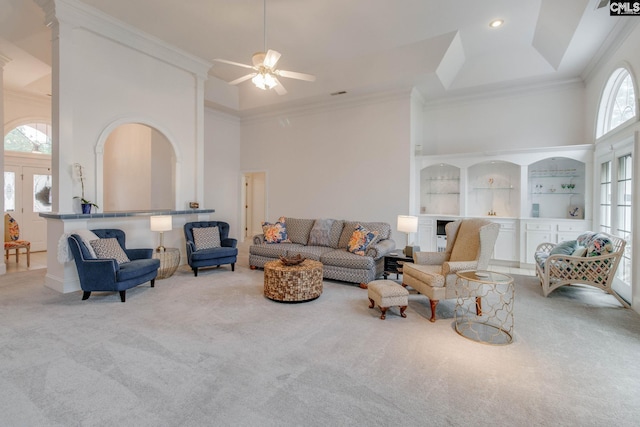 living room featuring ornamental molding, carpet floors, ceiling fan, and a towering ceiling