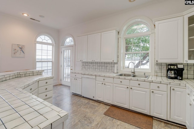 kitchen with white dishwasher, tile countertops, tasteful backsplash, and plenty of natural light