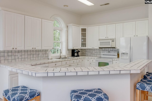 kitchen featuring tile counters, white appliances, a kitchen bar, and kitchen peninsula