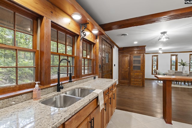 kitchen with light tile patterned floors, light stone counters, crown molding, and sink