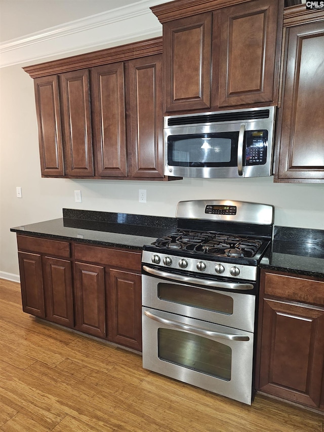 kitchen with dark brown cabinets, appliances with stainless steel finishes, dark stone countertops, and light wood-style flooring