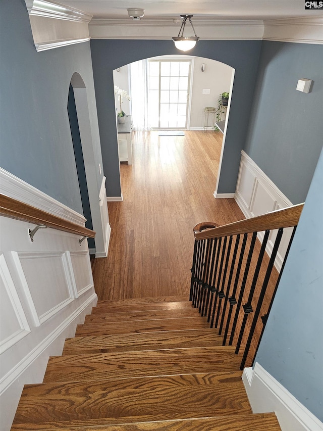 stairway with ornamental molding, arched walkways, baseboards, and wood finished floors