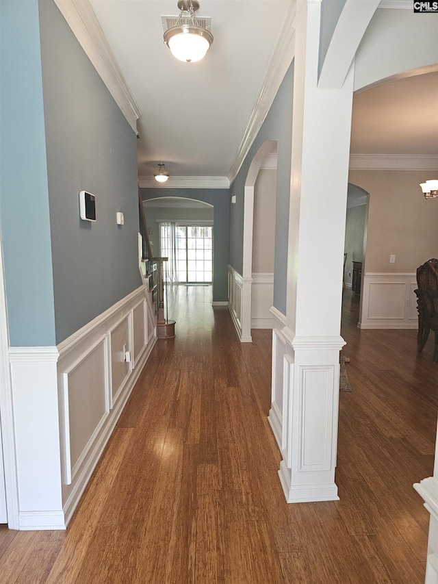 corridor with ornamental molding, arched walkways, and wood finished floors