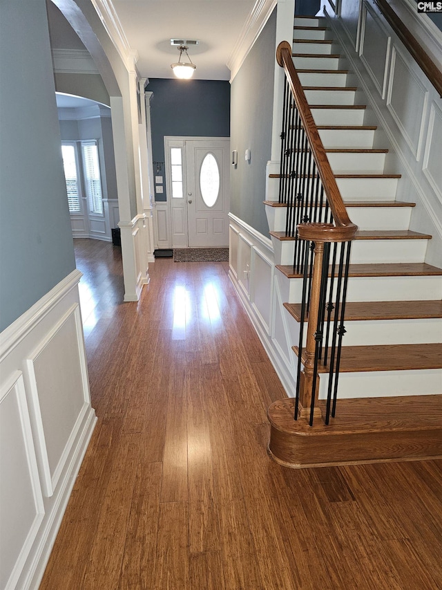 entryway featuring arched walkways, a decorative wall, wood finished floors, stairway, and crown molding