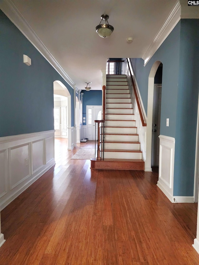 interior space with arched walkways, crown molding, stairway, wainscoting, and wood finished floors