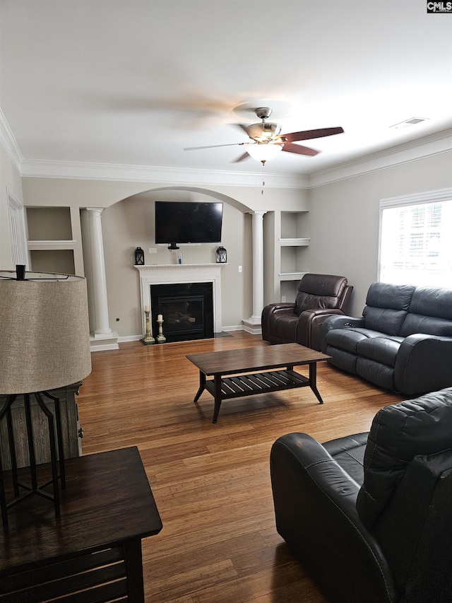 living room featuring built in shelves, visible vents, ornate columns, a glass covered fireplace, and crown molding