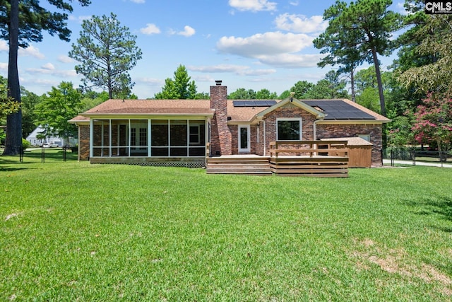 rear view of property featuring a lawn, a deck, a sunroom, and solar panels