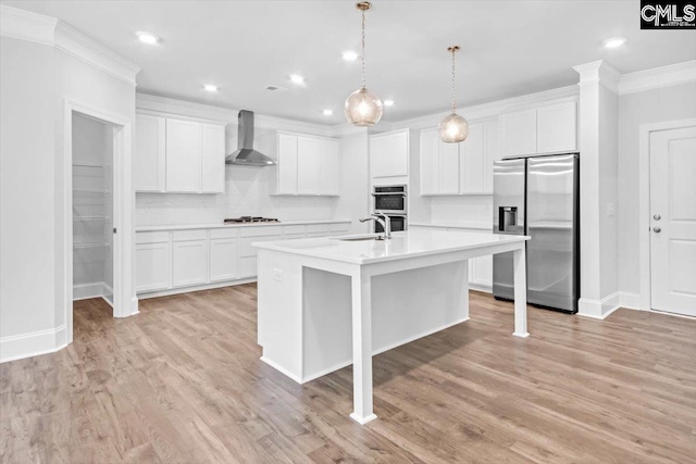 kitchen with a kitchen island with sink, ornamental molding, light countertops, appliances with stainless steel finishes, and wall chimney range hood