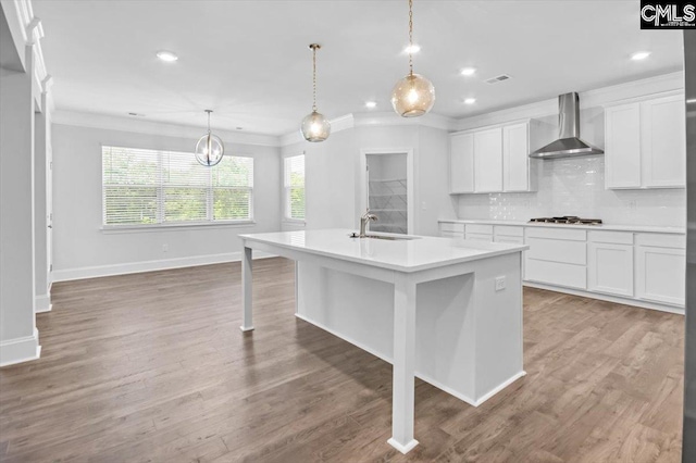 kitchen with a sink, wall chimney exhaust hood, crown molding, light countertops, and decorative backsplash