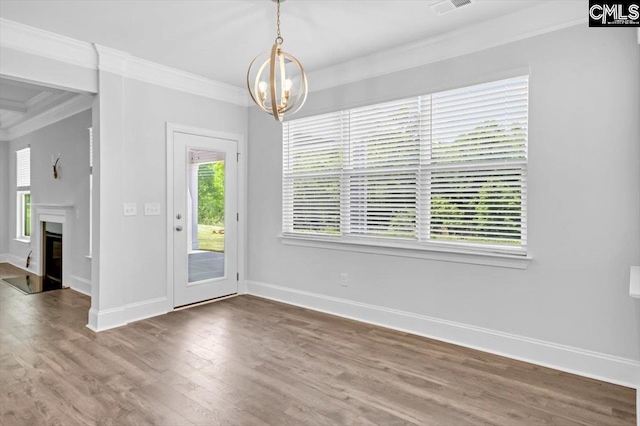 unfurnished dining area with baseboards, ornamental molding, an inviting chandelier, wood finished floors, and a glass covered fireplace