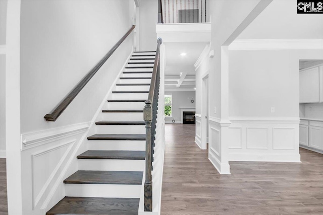 staircase with a decorative wall, a fireplace, wood finished floors, and ornamental molding