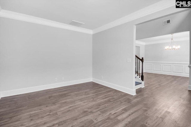 empty room with visible vents, wood finished floors, stairway, crown molding, and a chandelier