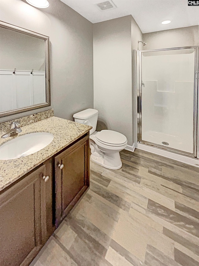 bathroom with wood-type flooring, walk in shower, vanity, and toilet