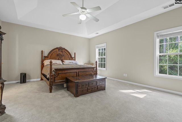 bedroom featuring a raised ceiling, ceiling fan, multiple windows, and light colored carpet