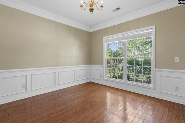 empty room with hardwood / wood-style flooring, an inviting chandelier, ornamental molding, and a wealth of natural light