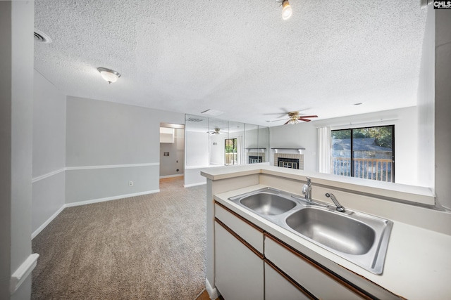 unfurnished living room featuring carpet, ceiling fan, a textured ceiling, and a brick fireplace