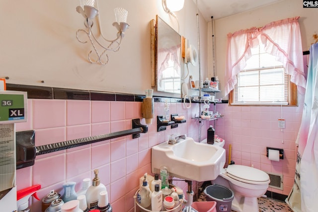 bathroom with toilet, sink, and tile walls