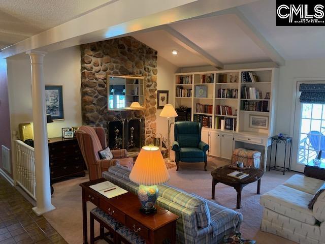 living room with decorative columns, a stone fireplace, and lofted ceiling with beams