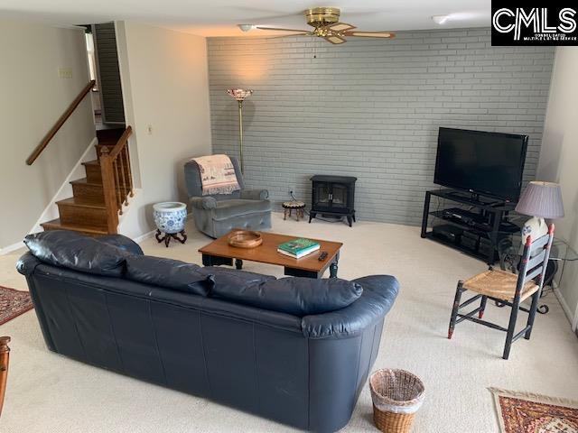 carpeted living room with a wood stove and ceiling fan