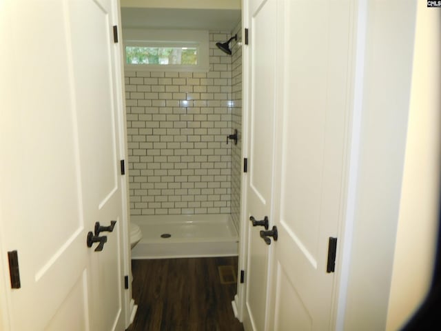 bathroom featuring toilet, hardwood / wood-style floors, and a tile shower