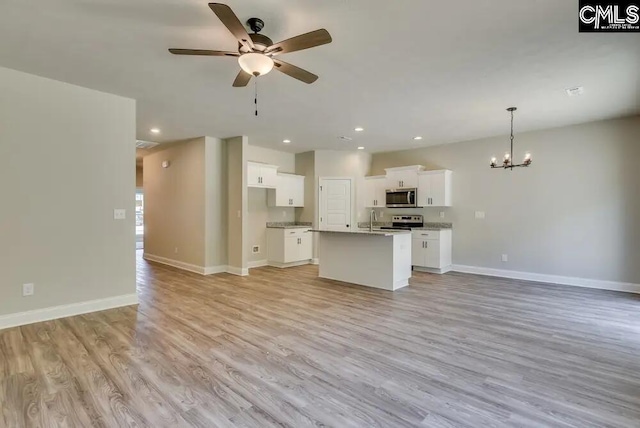 kitchen with decorative light fixtures, an island with sink, white cabinets, stainless steel appliances, and light hardwood / wood-style flooring