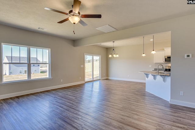 unfurnished living room with sink, dark wood-type flooring, a wealth of natural light, and ceiling fan with notable chandelier