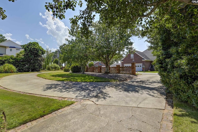 obstructed view of property with curved driveway, a front yard, and fence