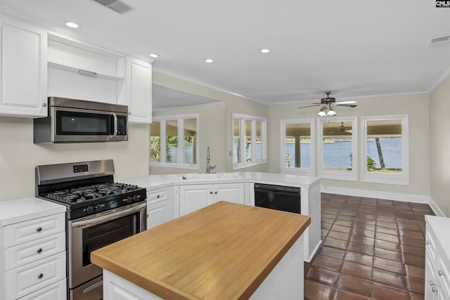 kitchen featuring butcher block counters, appliances with stainless steel finishes, ornamental molding, a peninsula, and a sink