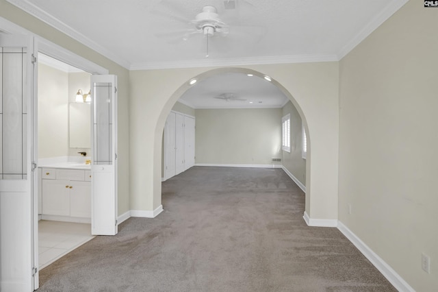 unfurnished room with arched walkways, ceiling fan, baseboards, and light colored carpet