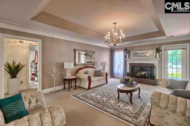 carpeted living room featuring crown molding, a chandelier, a tray ceiling, and a brick fireplace