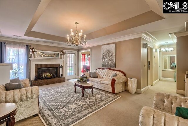 living room with an inviting chandelier, light colored carpet, a fireplace, a raised ceiling, and ornamental molding